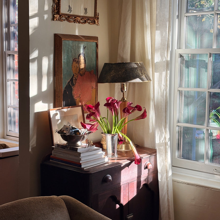 Burgundy calla lilies from Floral Post in a silver vase on a wooden dresser by a sunny window