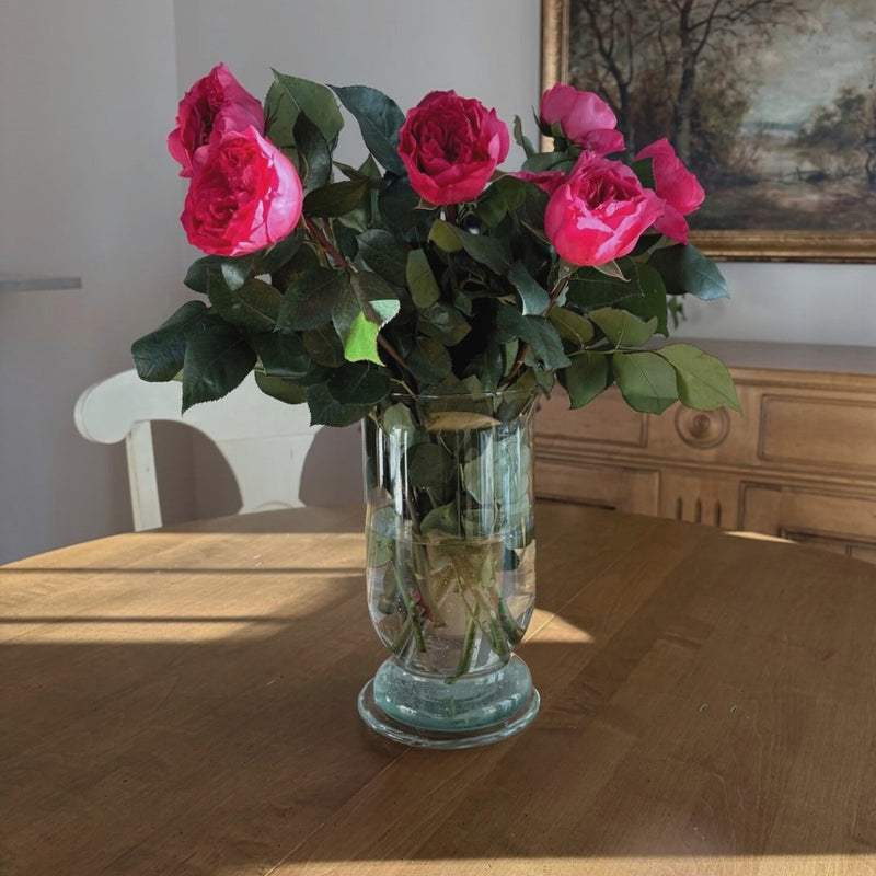 Pink garden roses in a glass vase on a sunlit dining table