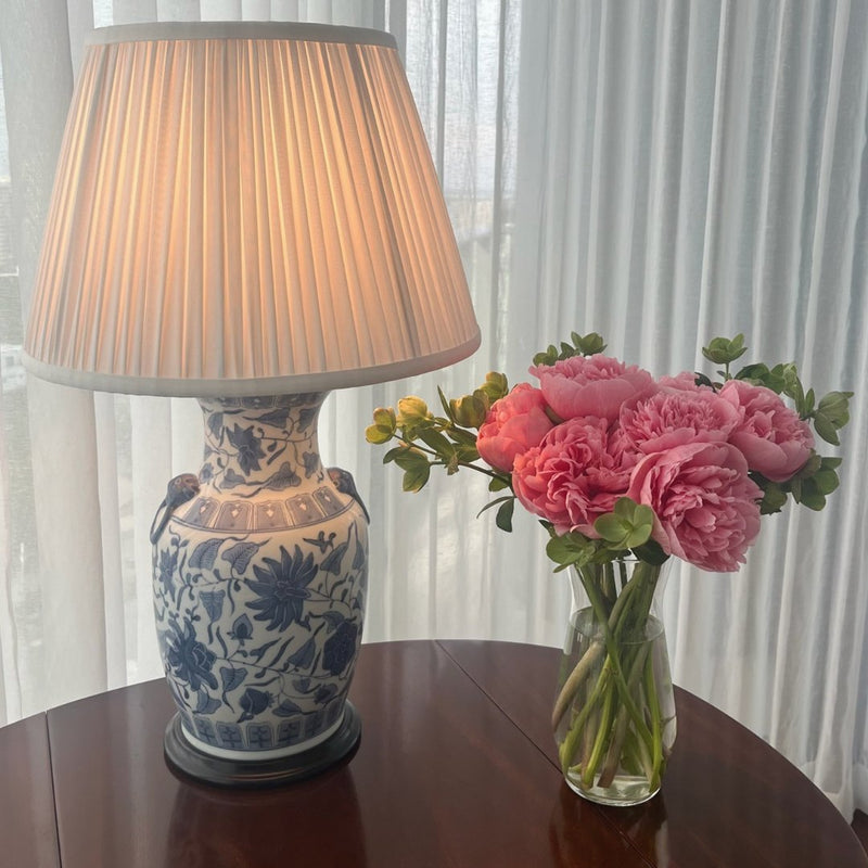 Pink peonies in a vase beside a blue and white lamp