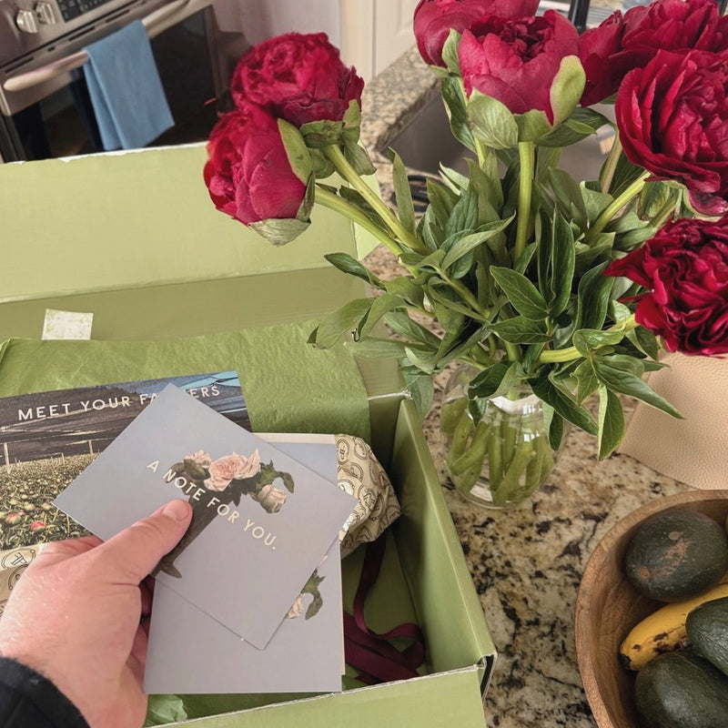 Red peonies in a vase next to an opened Floral Post box and note card